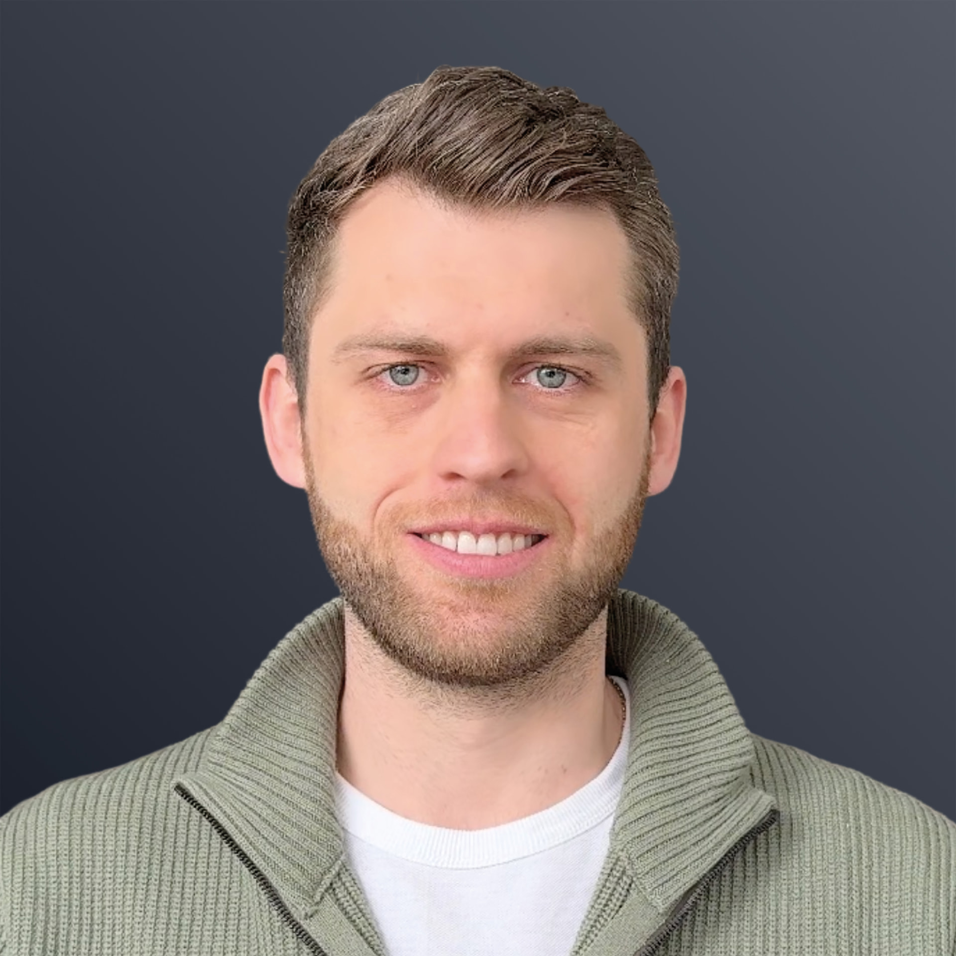 Porträt von Nicolas Müller, Head of Product Development bei in-manas: lächelnder Mann mit kurzem Bart und grünem Strickpullover vor dunklem Hintergrund